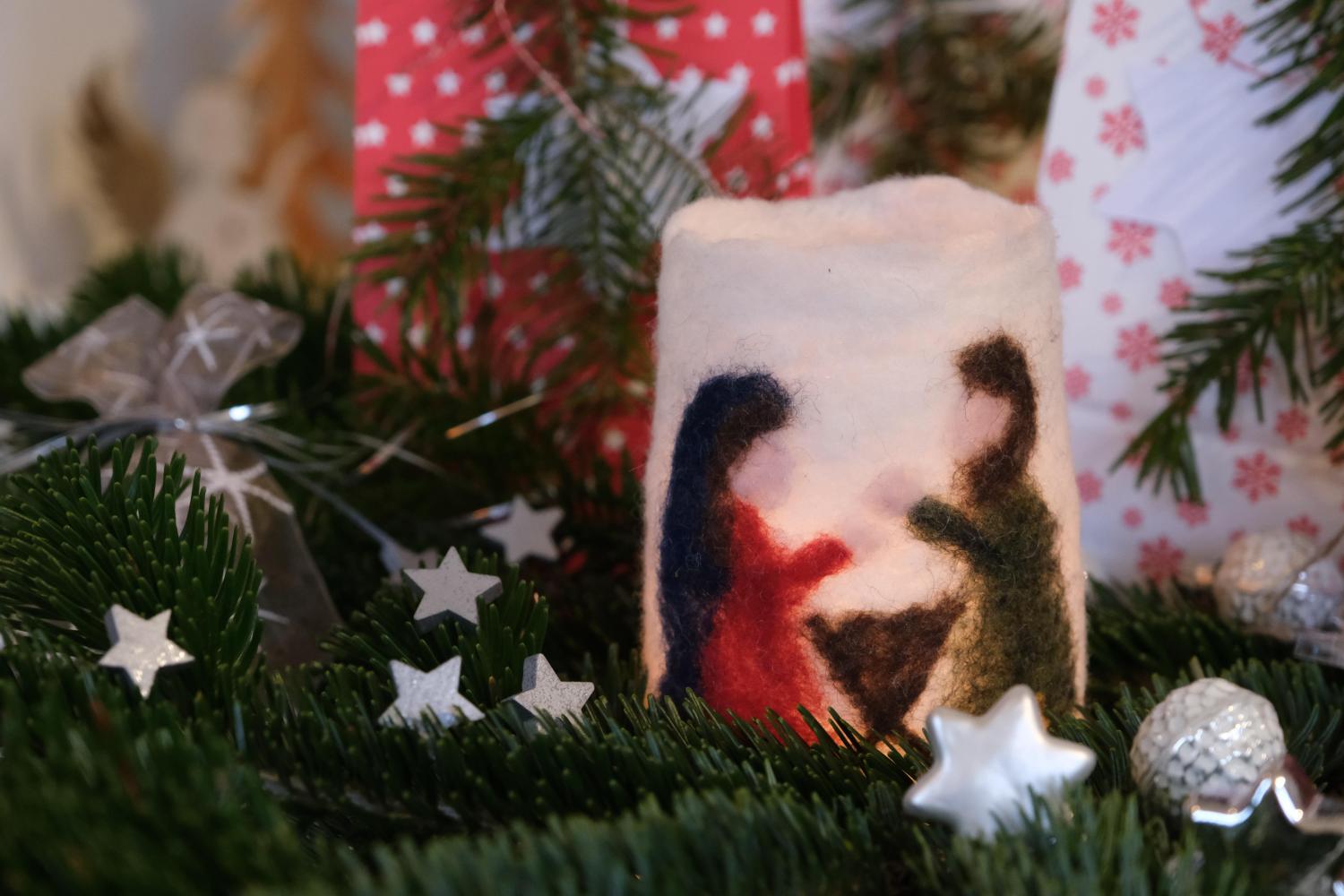 Filzkerze mit Krippenszene zwischen Tannenzweigen und Weihnachtsdekoration